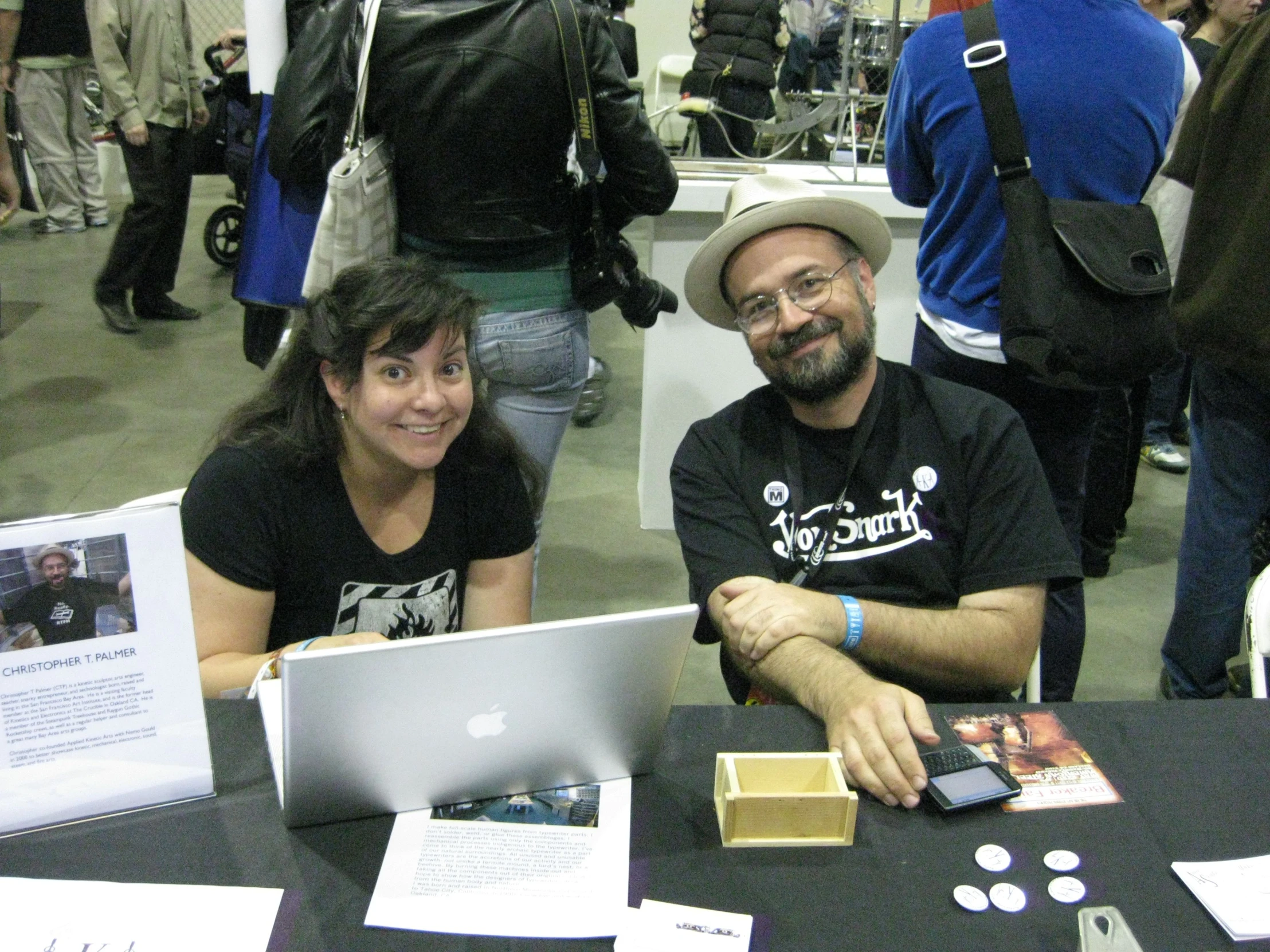 two people sit smiling at a table with their laptops