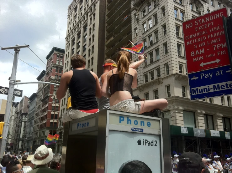 women sitting on top of a phone booth in front of a crowd