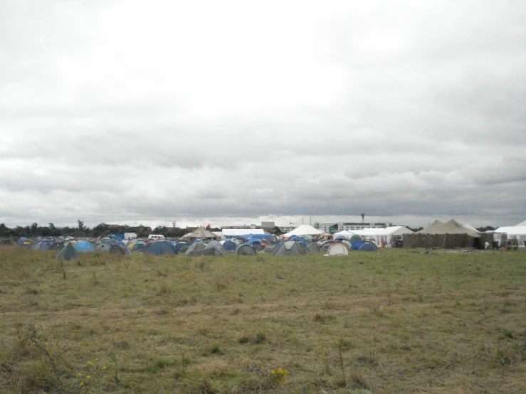 a grassy field with many tents and cars parked in the back ground