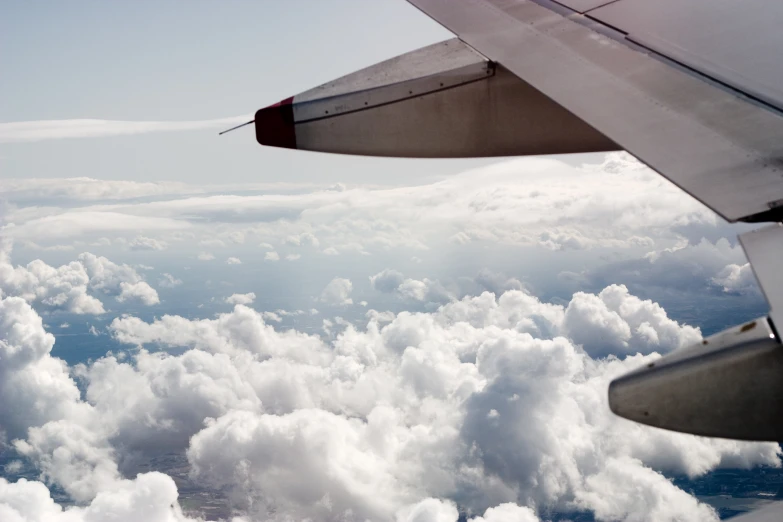 an airplane wing flying over some clouds with another plane in the distance