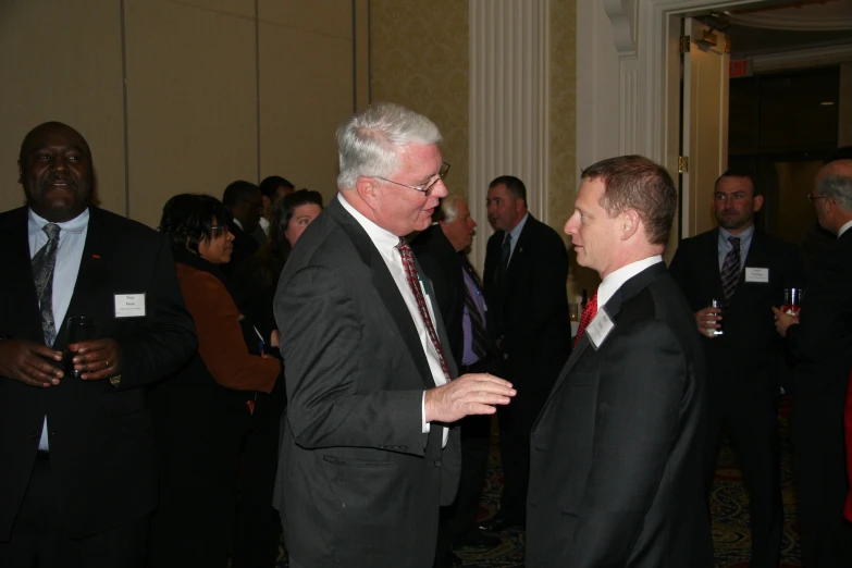 two men in suits talking in front of some other people