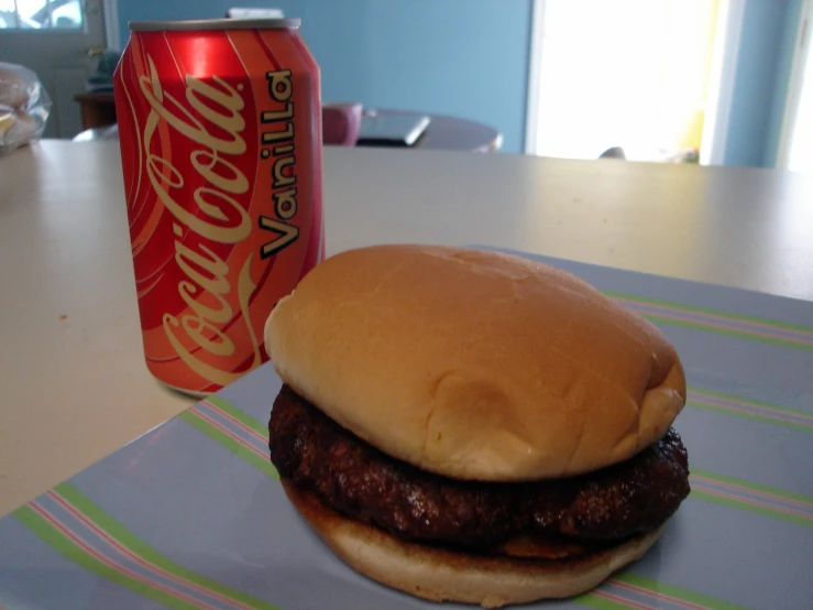 a hamburger sits on a plate next to a can of soda