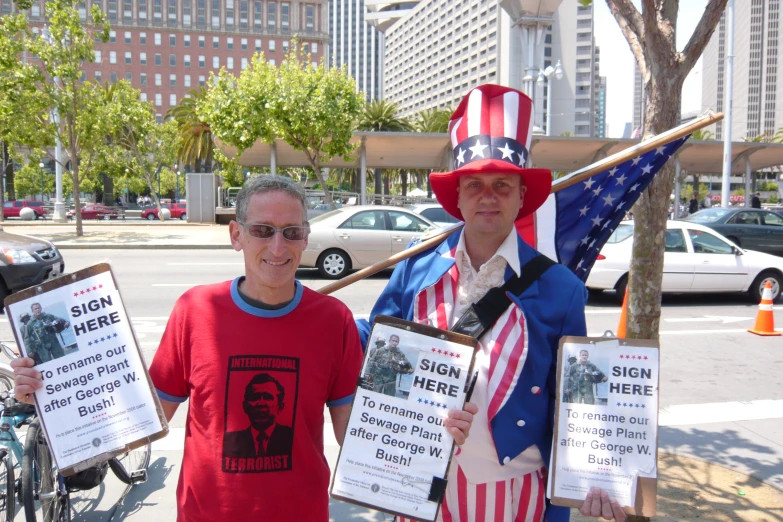 two men stand holding up political signs next to a tree