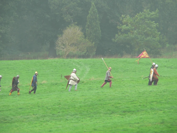 people standing in the grass with their backs to the camera, a man holding a flag and throwing water at them, while another person holds a baseball bat