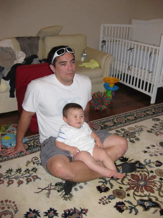 man holding baby sitting on rug in room