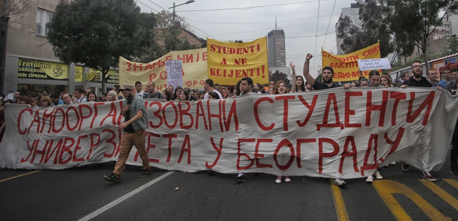 several people holding a banner in a street while a crowd stands behind them