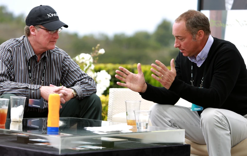 the man in black jacket is talking with another man at a table