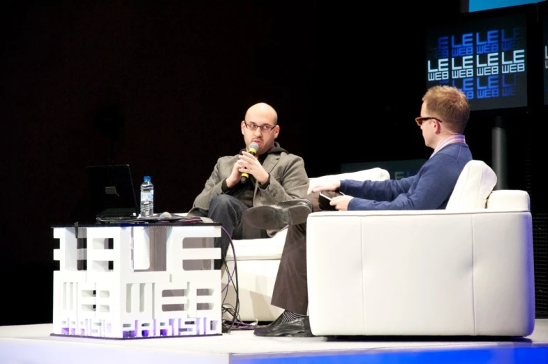 two people sitting in chairs, one is speaking and the other has a microphone