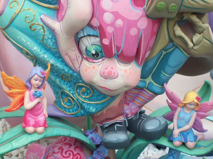 a pink and blue bear statue with two little fairy figures