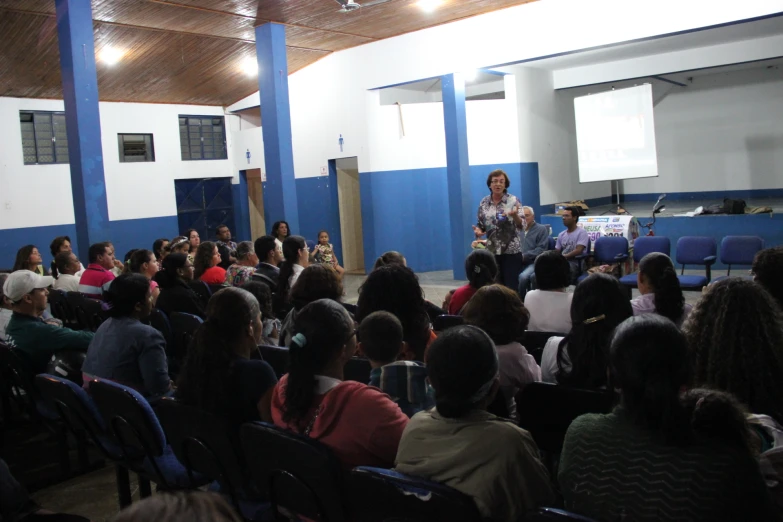 many people sitting in chairs listening to a man on a stage