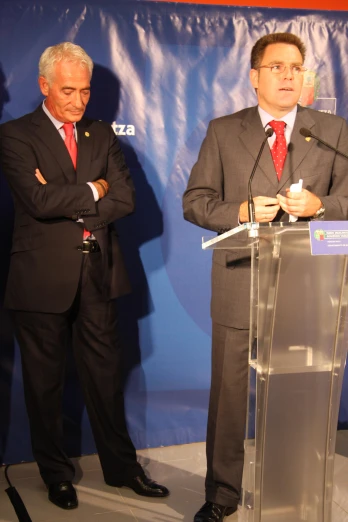 two men standing next to each other while speaking into microphones