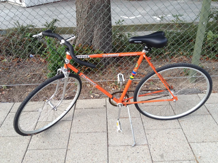 a bicycle sits on a sidewalk next to a chain linked fence