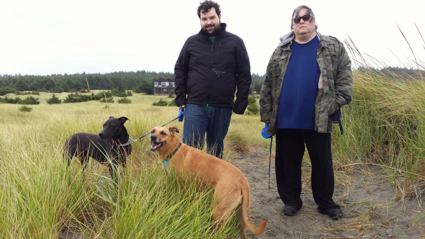 two men standing next to a dog in a field