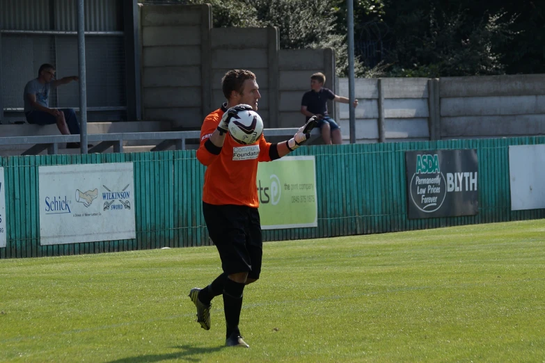 man in orange jacket holding up white and black soccer ball