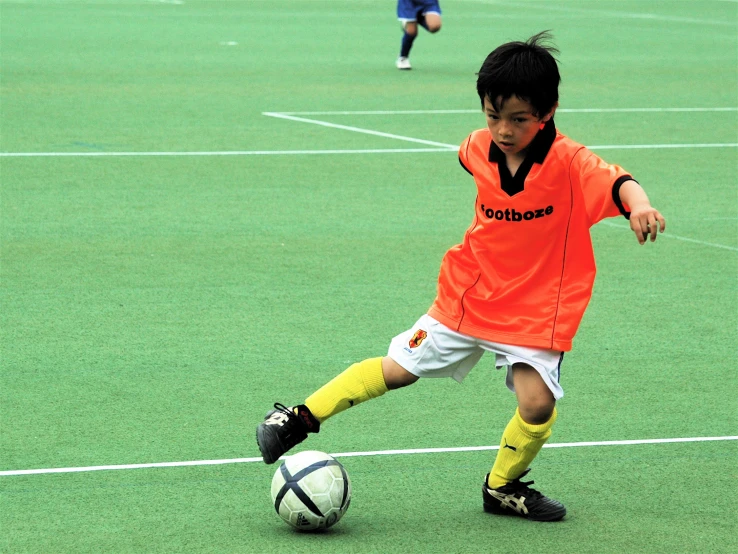 a child wearing an orange soccer shirt dribbles a soccer ball