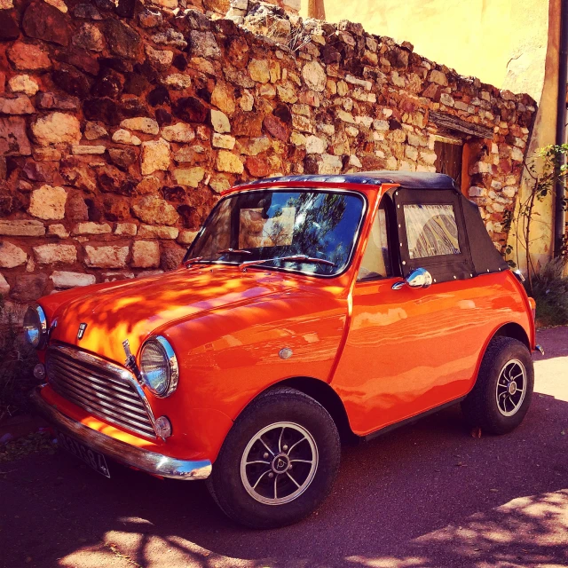 a car is painted orange while parked next to a stone wall