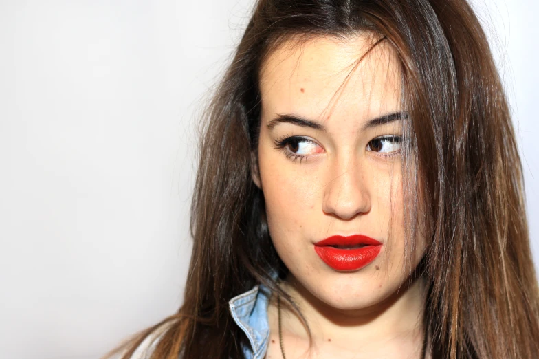 a beautiful young woman with red lipstick holding her hair in the wind