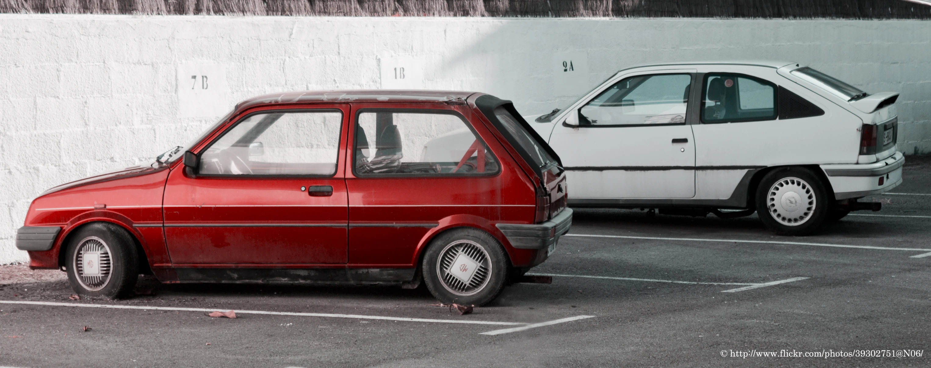 an old, red car in a parking space with an older style white car behind it