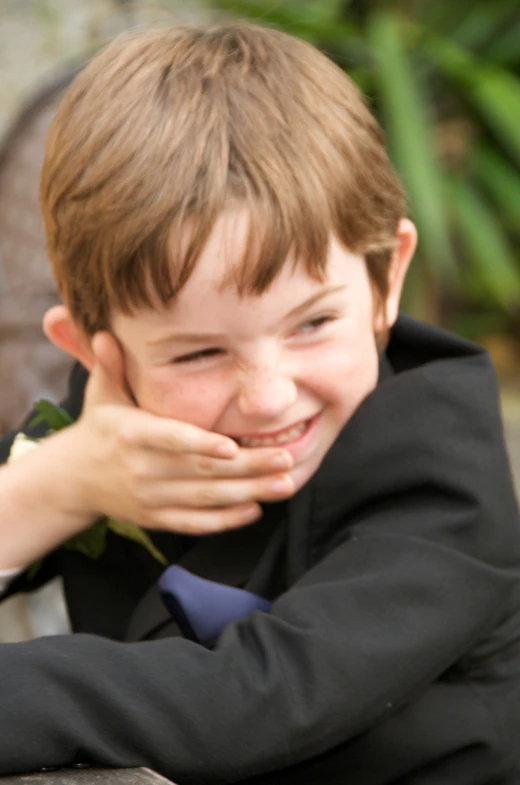 a boy in suit smiling while sitting on a bench