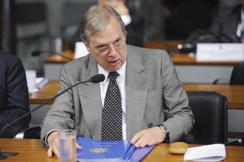 a man sits at a table with a blue folder in front of him