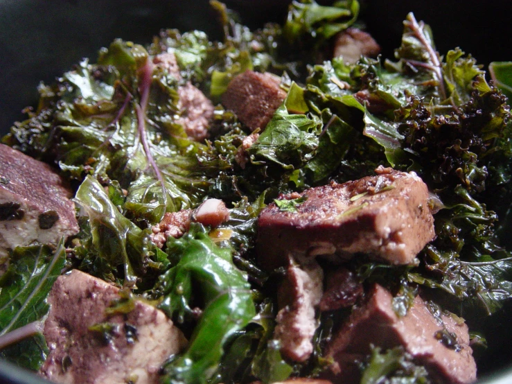 food is prepared with greens and meats in a bowl