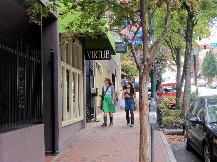 two women walking on a sidewalk past a small tree