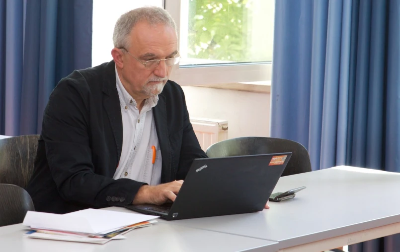 an older man sits at a desk using his laptop