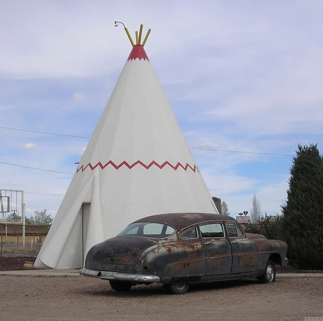 an old car parked in front of a teepee