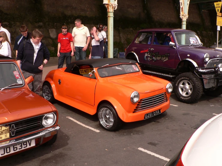 an orange convertible car is parked in front of another red convertible