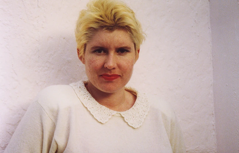 a blond woman with red lipstick standing in front of a white wall