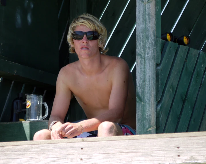 a man sitting on top of a wooden bench in shades