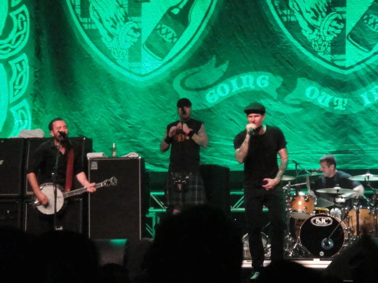 two musicians on stage in front of a large green wall