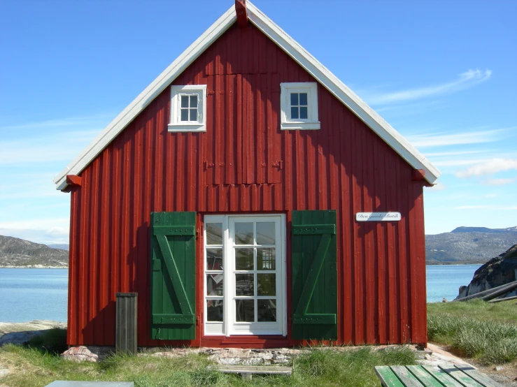 a red house with green shutters sitting on the side