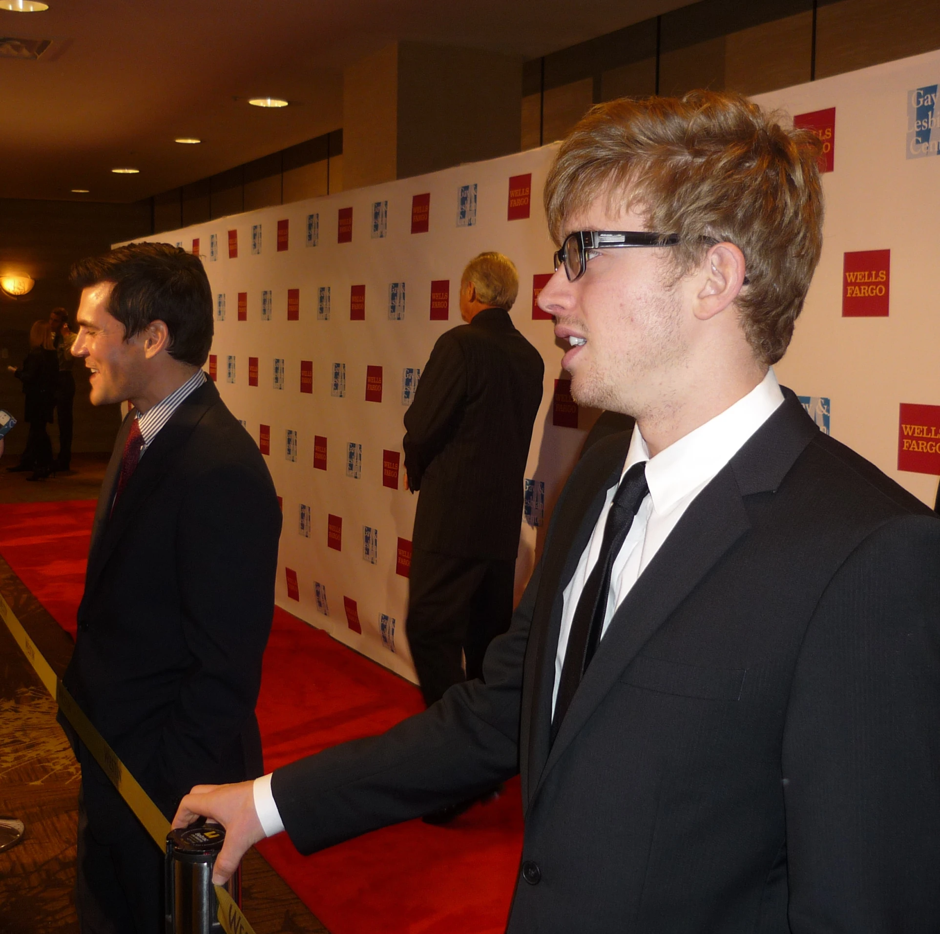two men in suits are talking on the red carpet