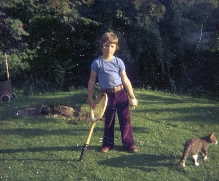 a young man holding a bat and a cat in a yard