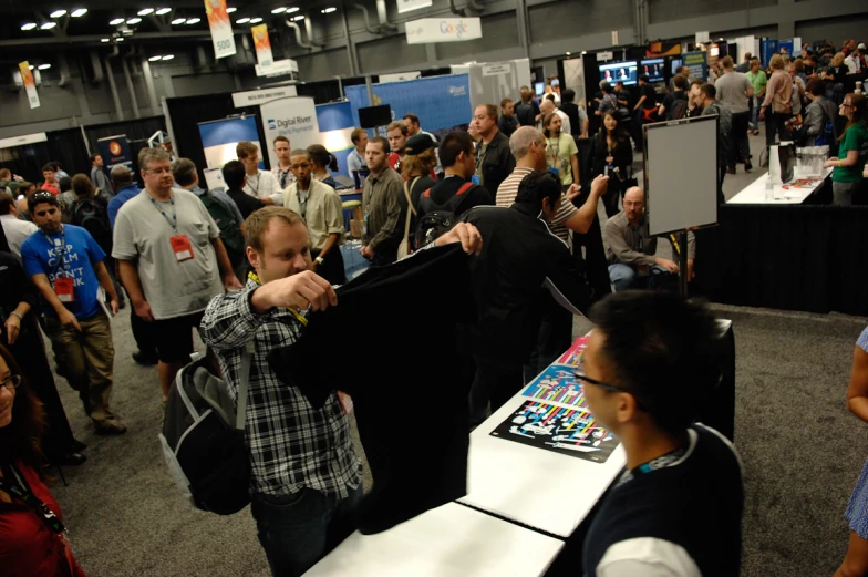 a bunch of people at a convention looking at a black shirt