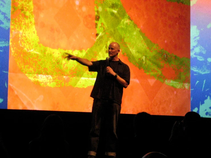 the man in the black shirt is standing on a stage giving a presentation