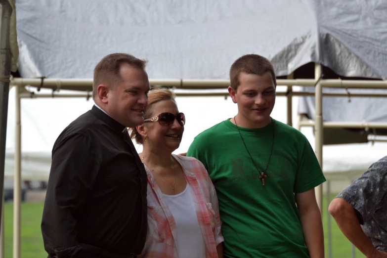 three people smiling and standing in front of a tent