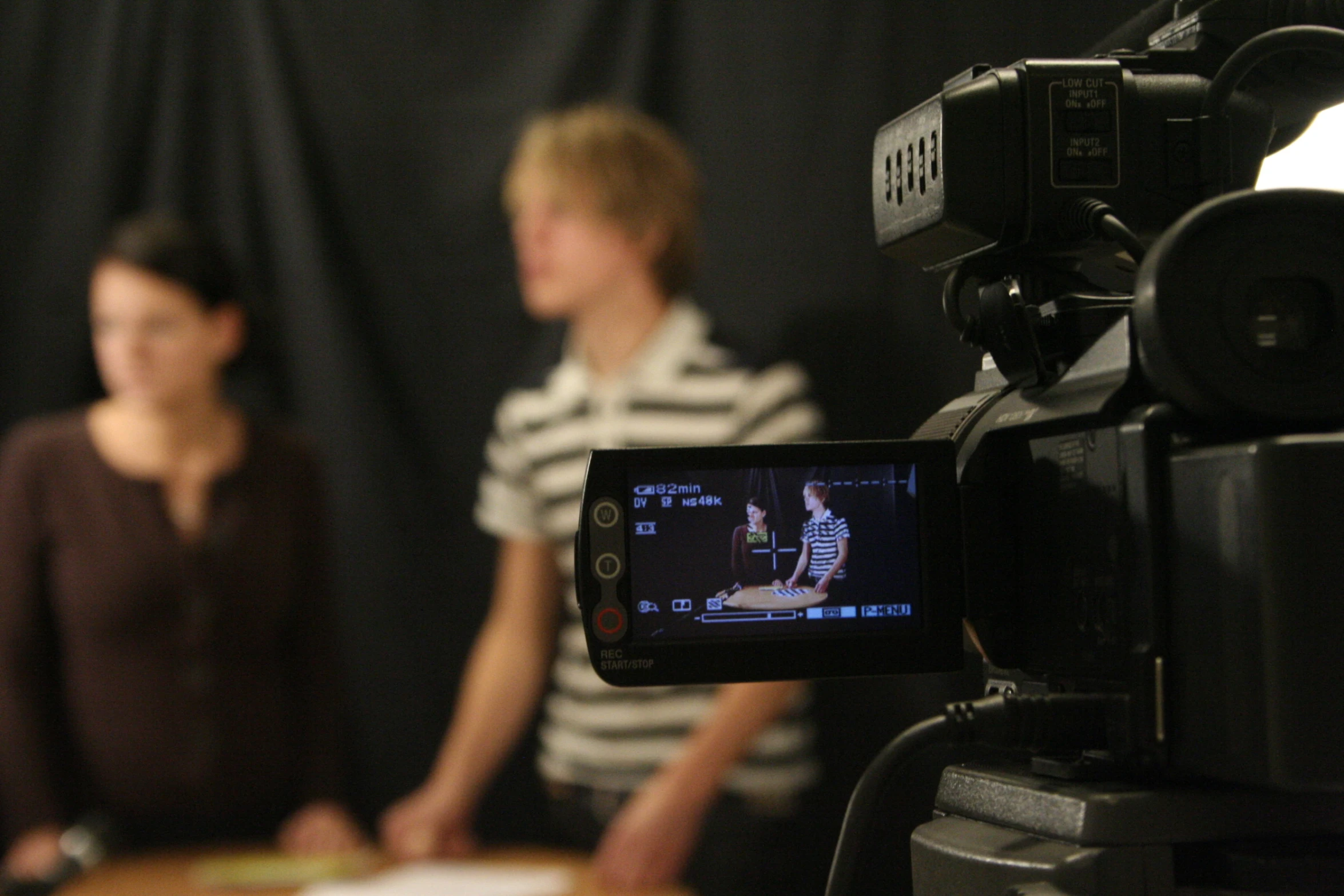 two people sit behind a camera set up