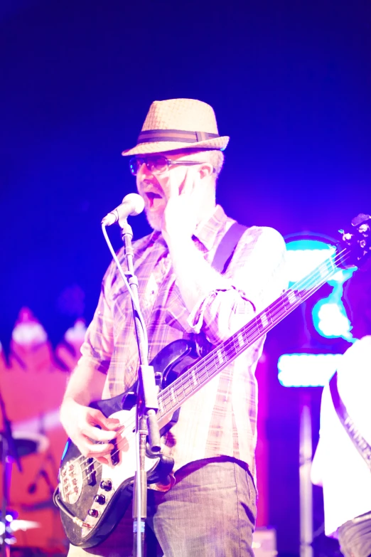 a man with a hat on playing bass while a crowd looks at him