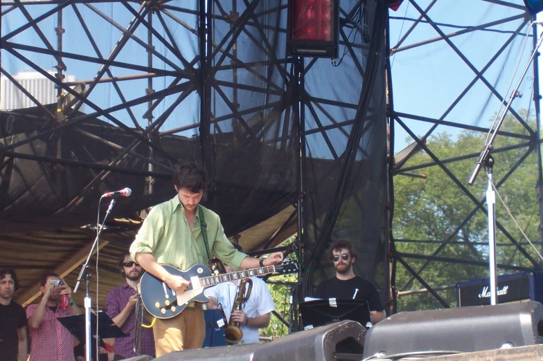 a man in green shirt playing a guitar at an outdoor concert