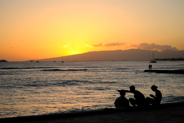 a couple of people sitting on top of a beach at sunset