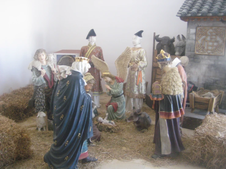 several statues of people dressed in clothing and hats standing near a barn