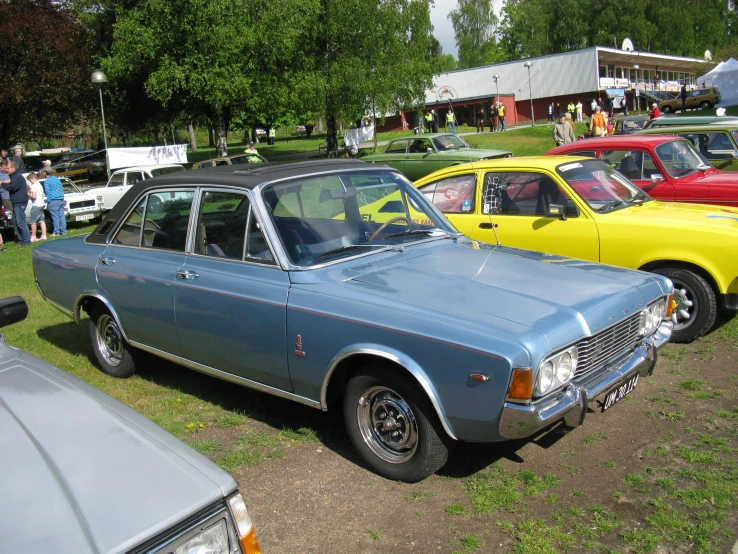 several different cars parked in the grass with people in the background