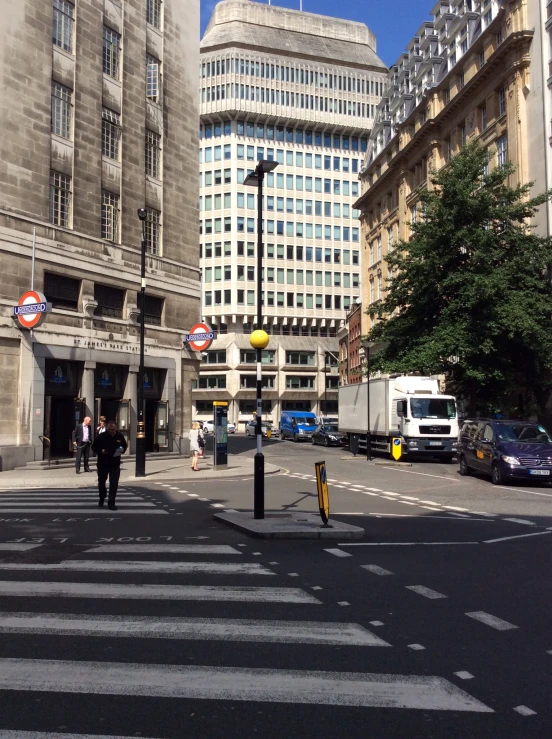 there are people walking around the crosswalks and in the background is tall buildings