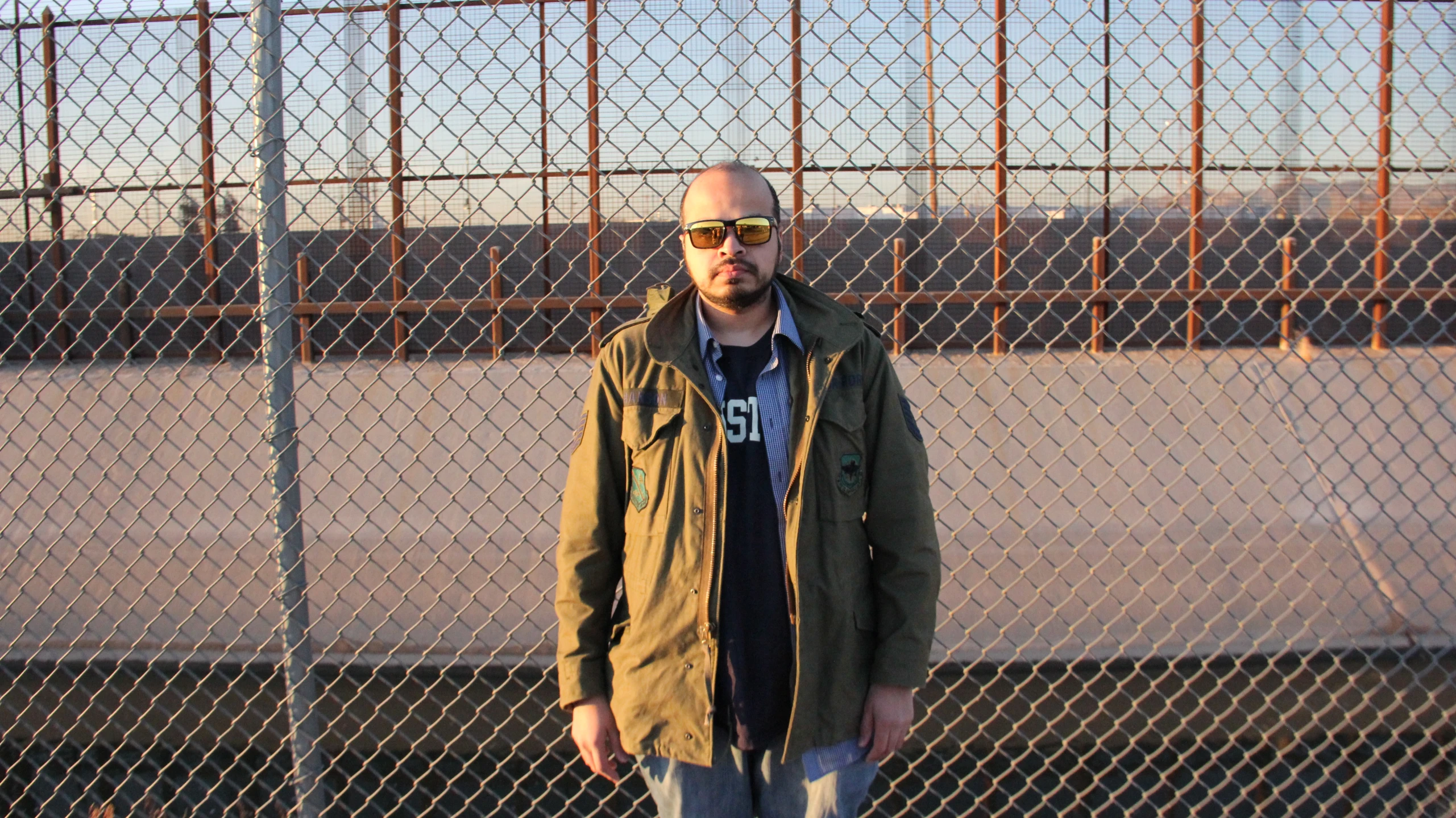 man in blue jeans and jacket standing next to fence