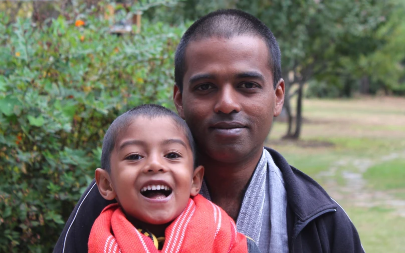 a man smiles at the camera while he holds a small boy