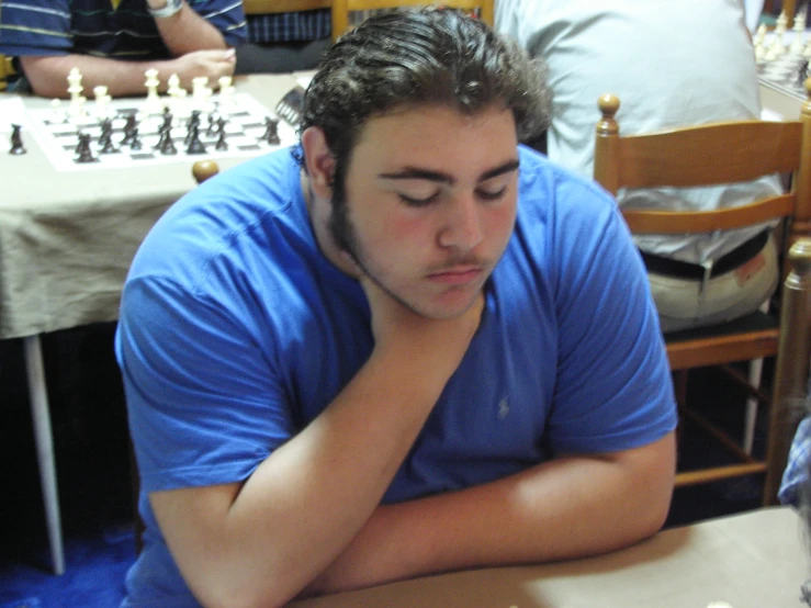 a young man sitting at a table with chess on it