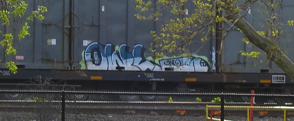 a cargo train with graffiti on it sitting near a tree