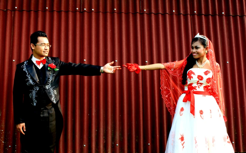 a bride and groom standing in front of a red metal fence